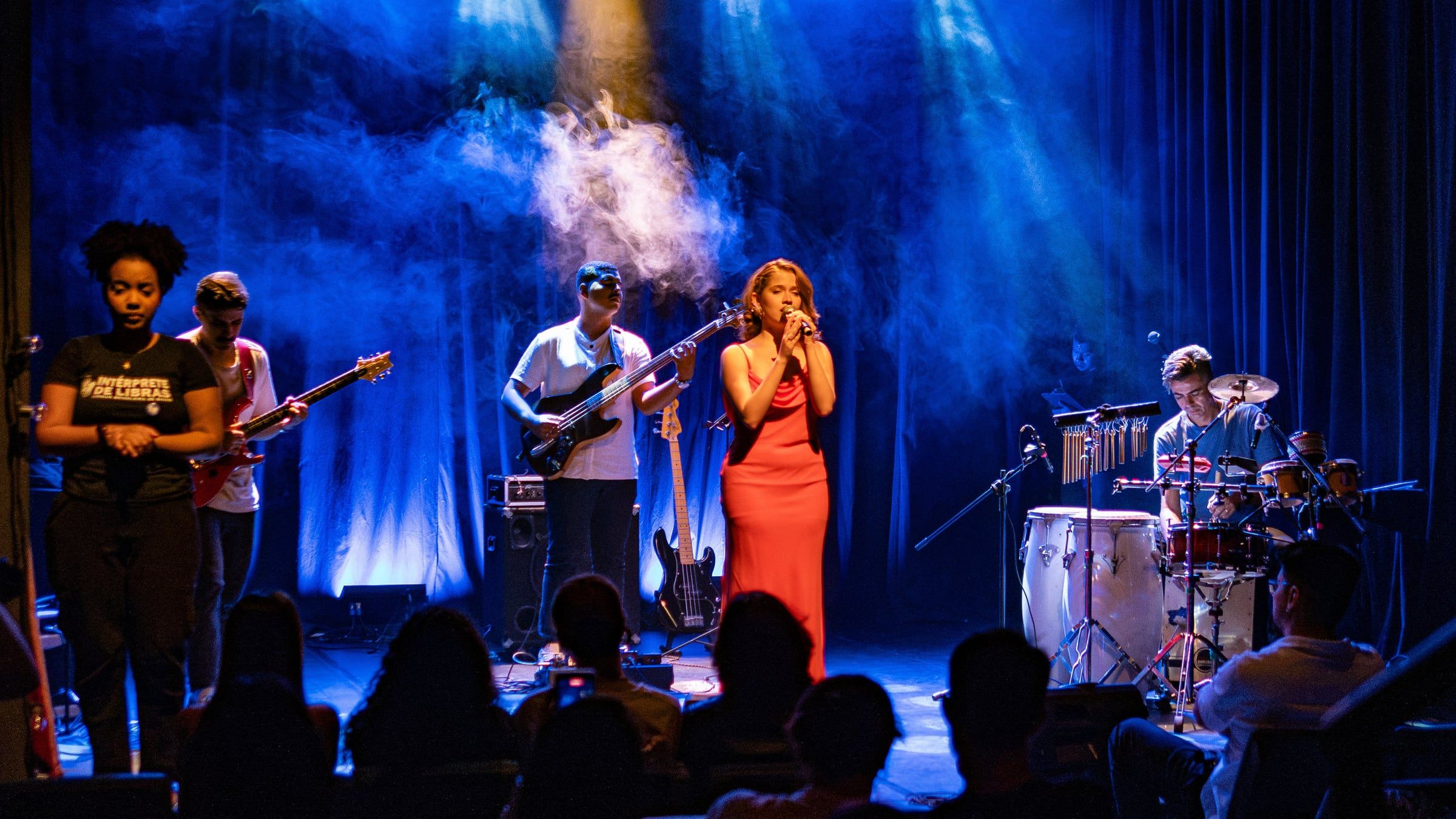 Show Calêndula: banda e cantora no palco do Theatro Homerinho sob luz azul