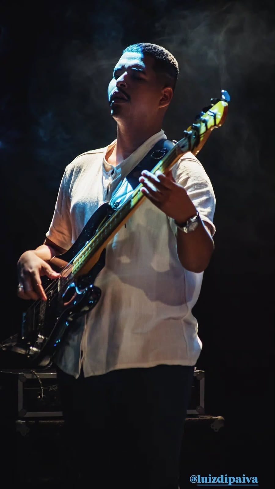 Luiz Guilherme no baixo elétrico olhando para o alto, em meio à fumaça de palco